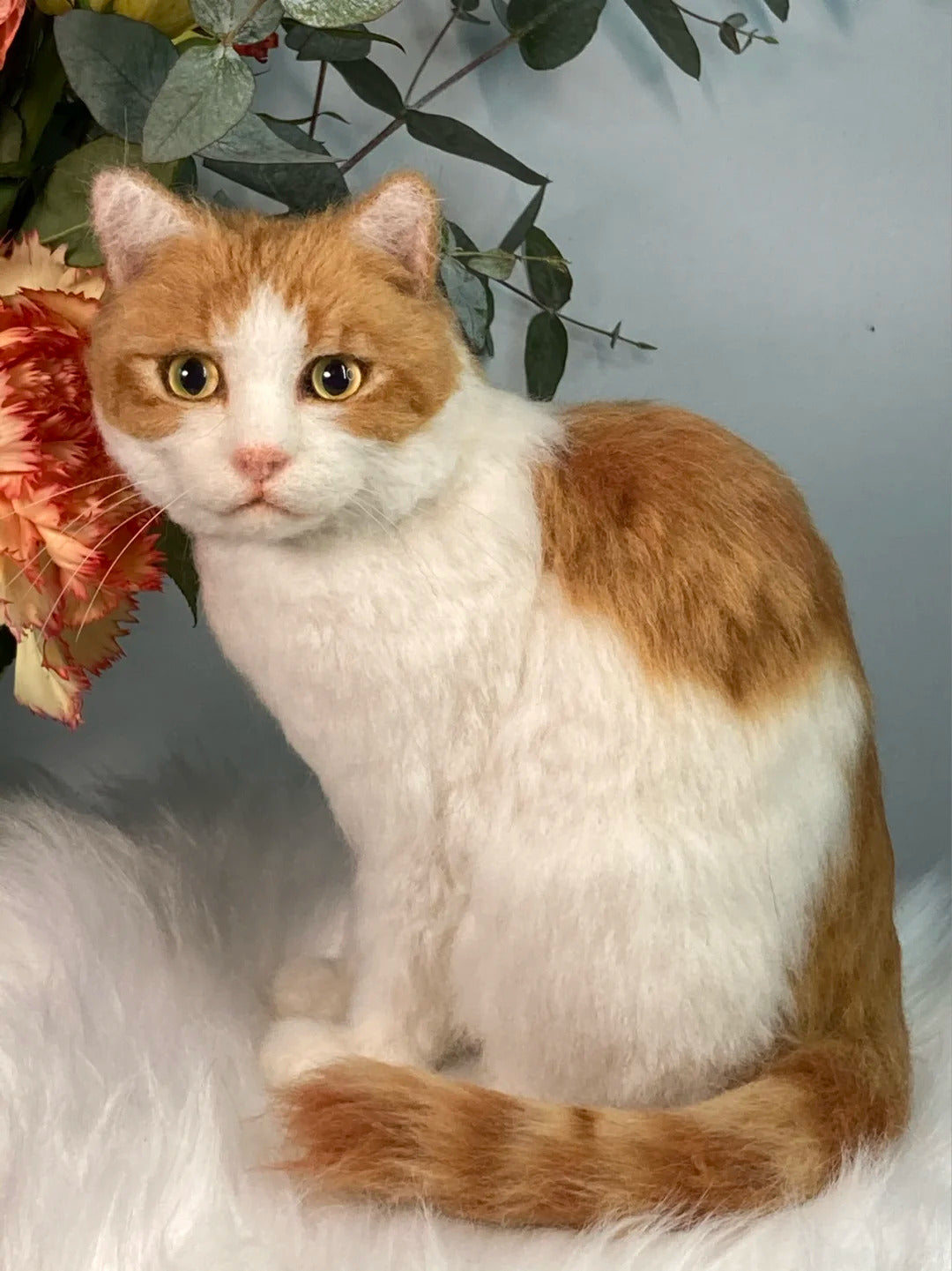 Orange and white cat sitting on a fluffy surface with flowers and greenery in the background