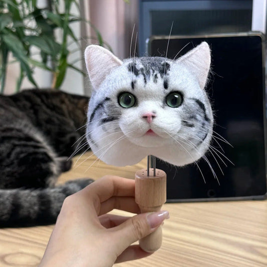 Cat-shaped toy held by a hand on a wooden surface with a cat in the background.