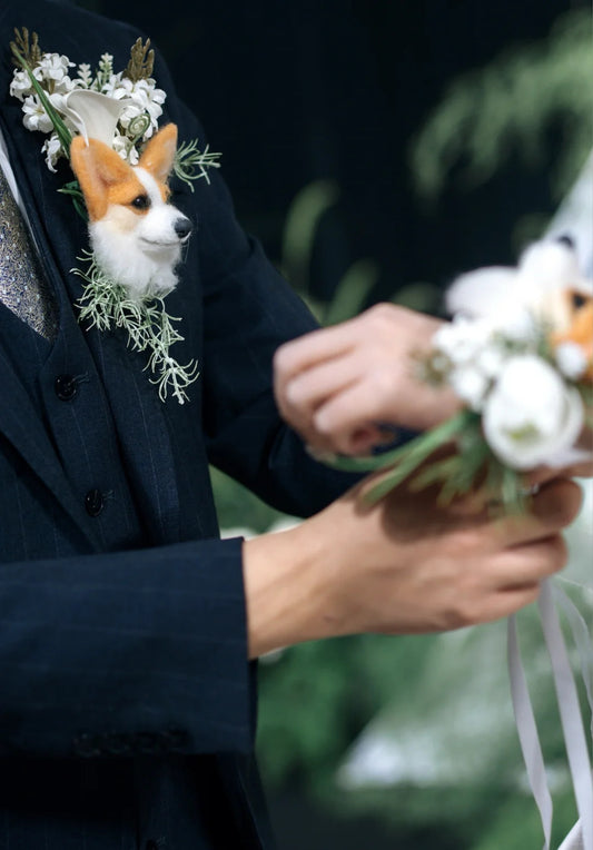 Person in a suit with a corgi dog wearing a floral collar, holding flowers.