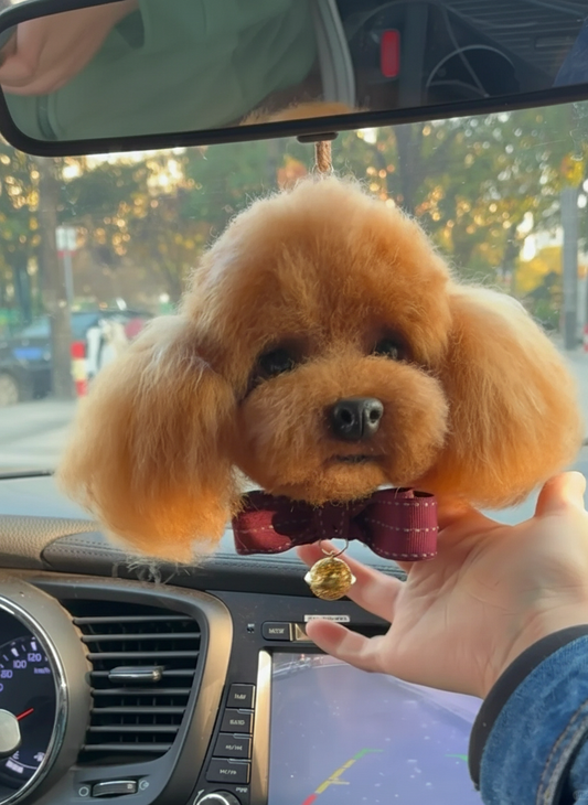 Small brown dog toy with a red bow tie held by a hand inside a car.