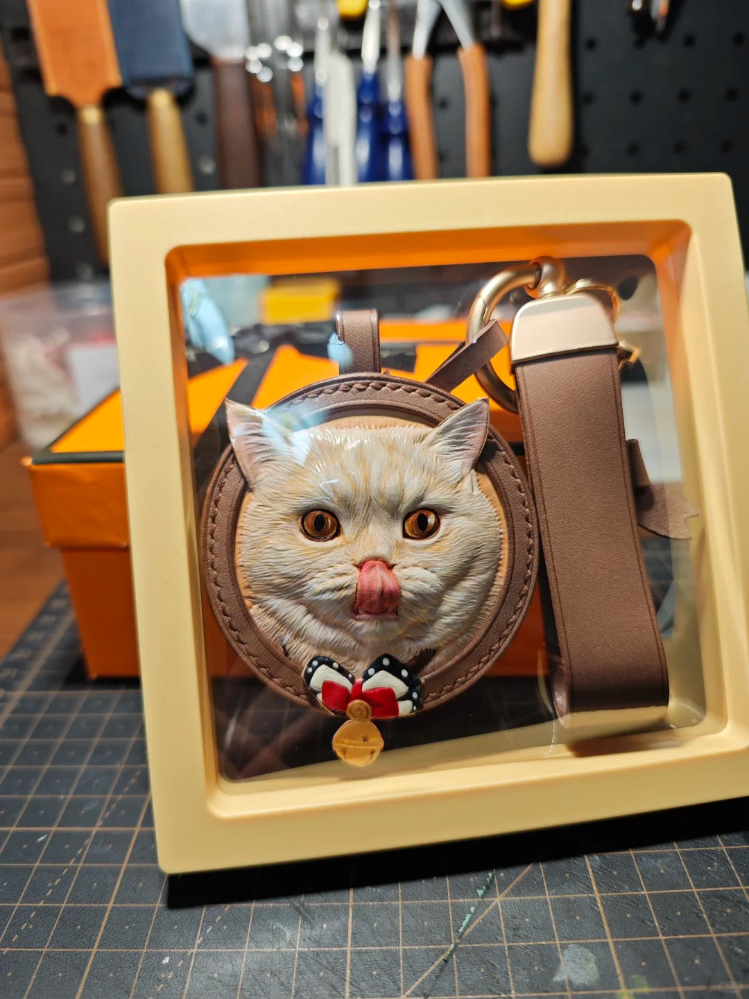 Cat-shaped keychain with a strap in a display case, with tools in the background.