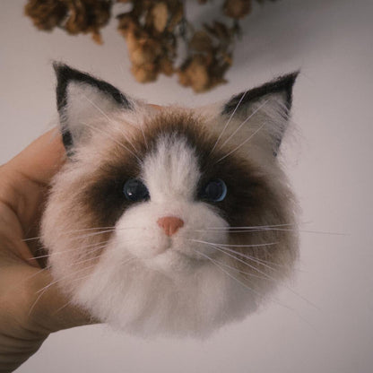 Cat-shaped plush toy held by a hand with dried flowers in the background
