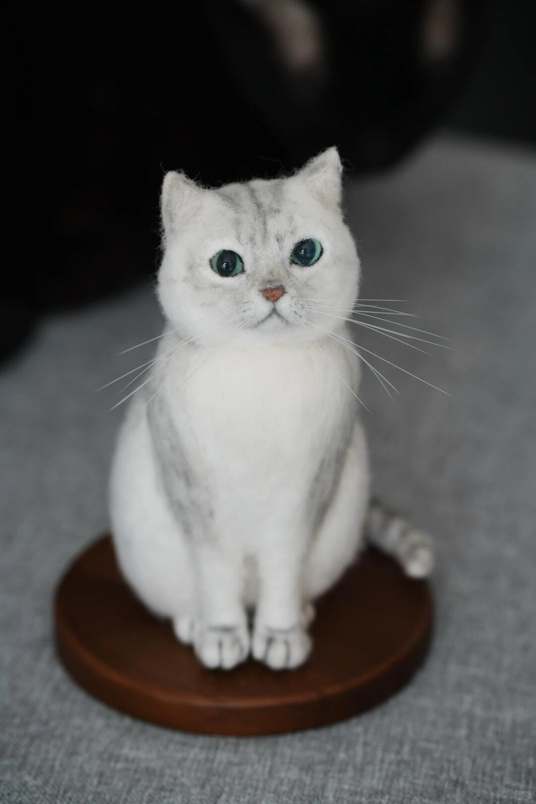 White cat figurine on a brown round base against a gray background