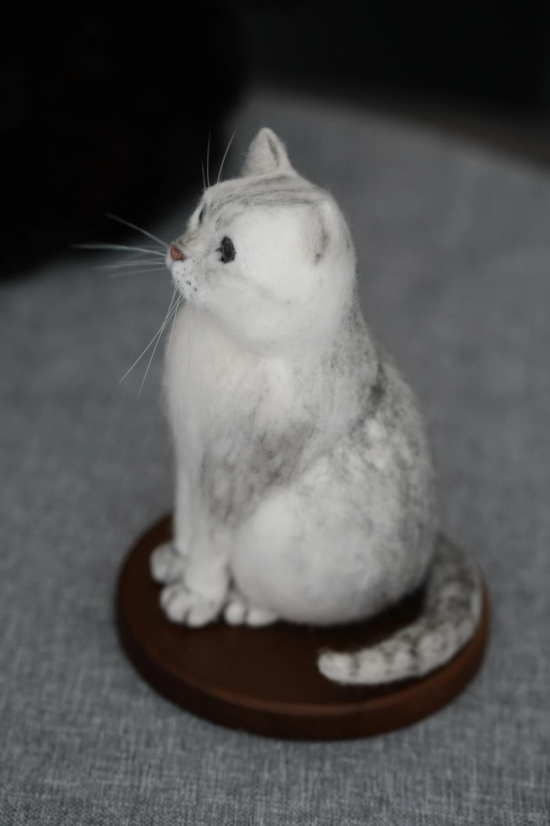 Felted sculpture of a gray cat on a dark brown stand against a gray background