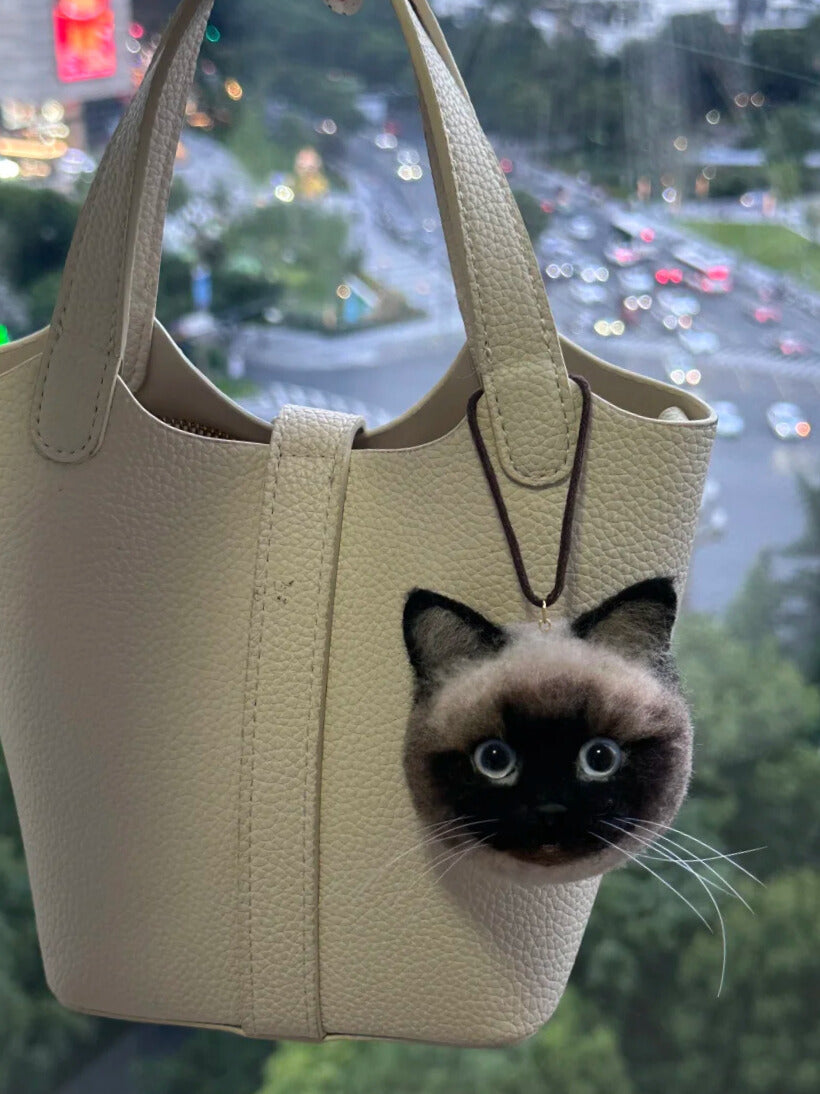 Beige handbag with a cat face design against a blurred cityscape background