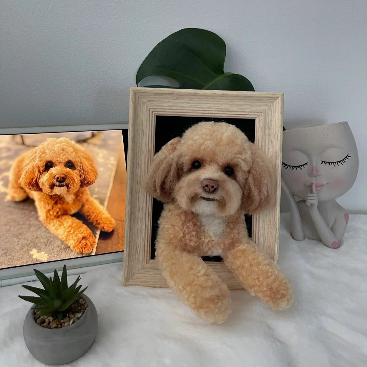Stuffed dog toy in a wooden frame with a plant and decorative item on a surface.