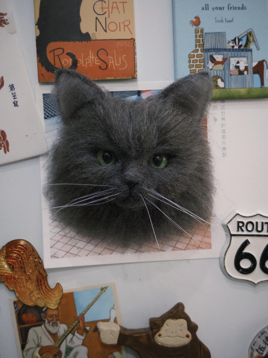 Gray cat head magnet on a refrigerator with various magnets and posters