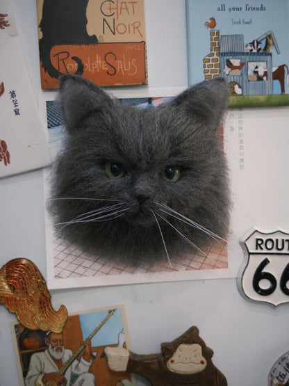 Gray cat head magnet on a refrigerator with various magnets and posters