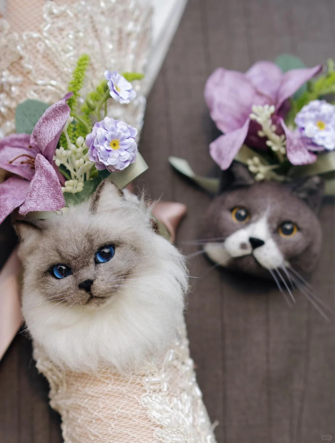 Two cats wearing flower crowns, one in a wedding dress, on a wooden floor.