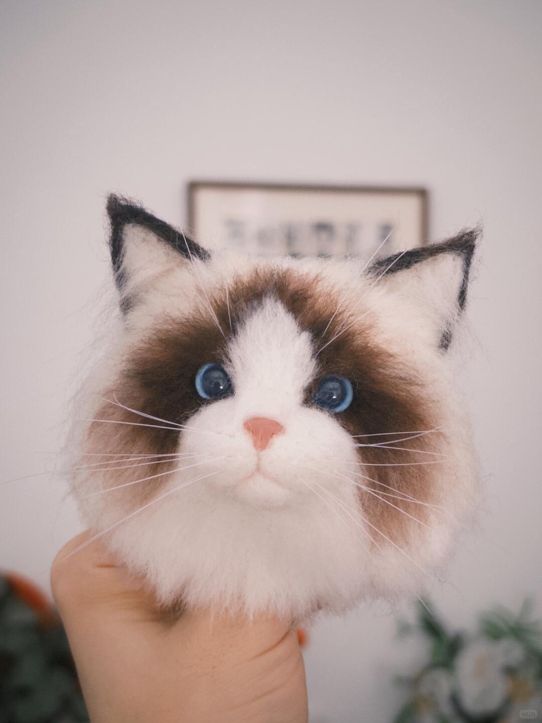 Stuffed cat toy with a realistic face held by a hand against a neutral background