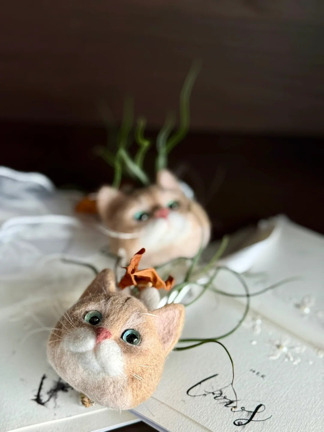 Two small cat figurines on a white surface with a blurred background