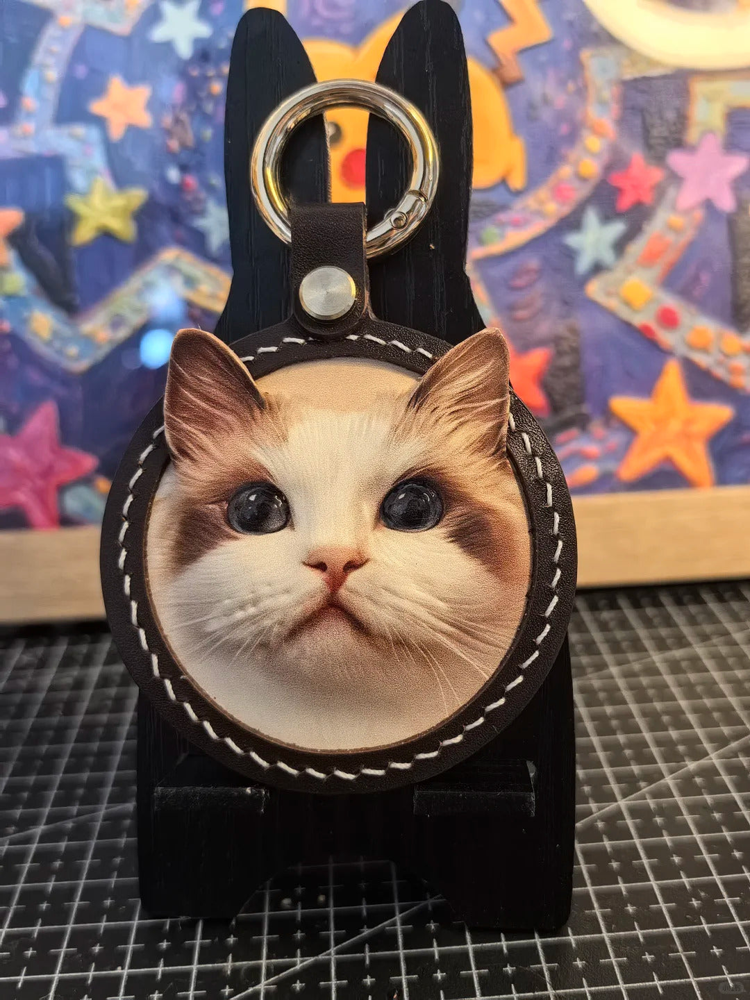 Keychain with a cat's face design on a colorful star-patterned background