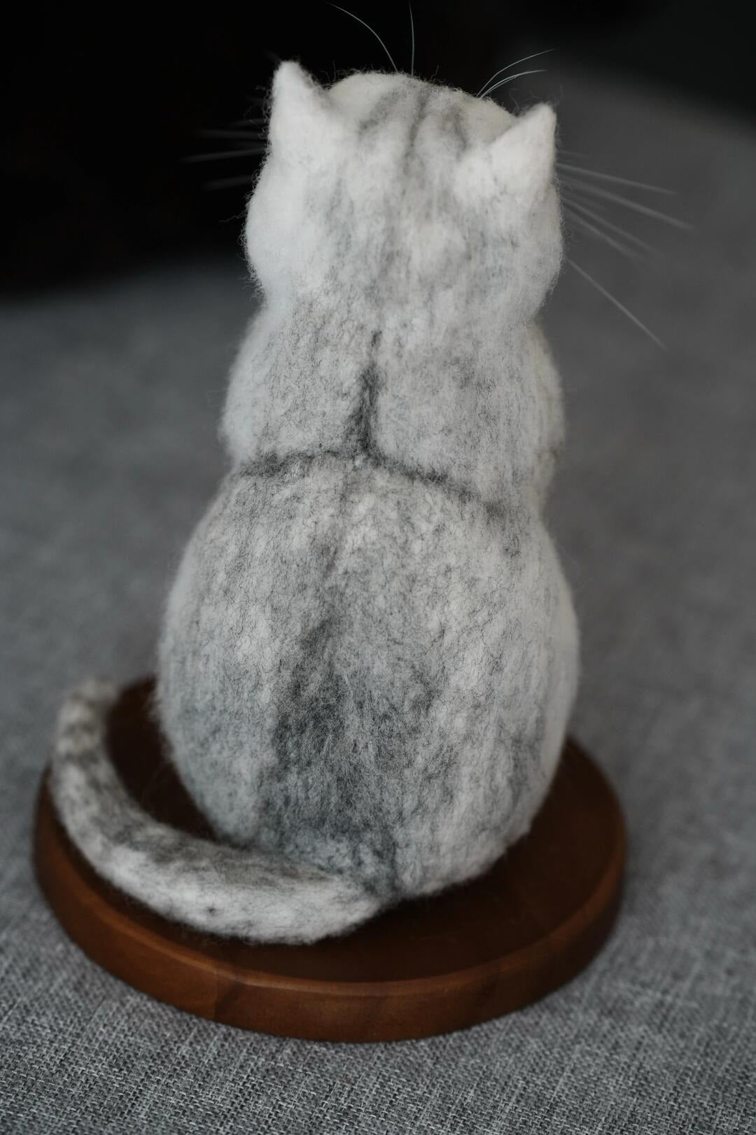 Felted cat sculpture on a wooden base against a gray background